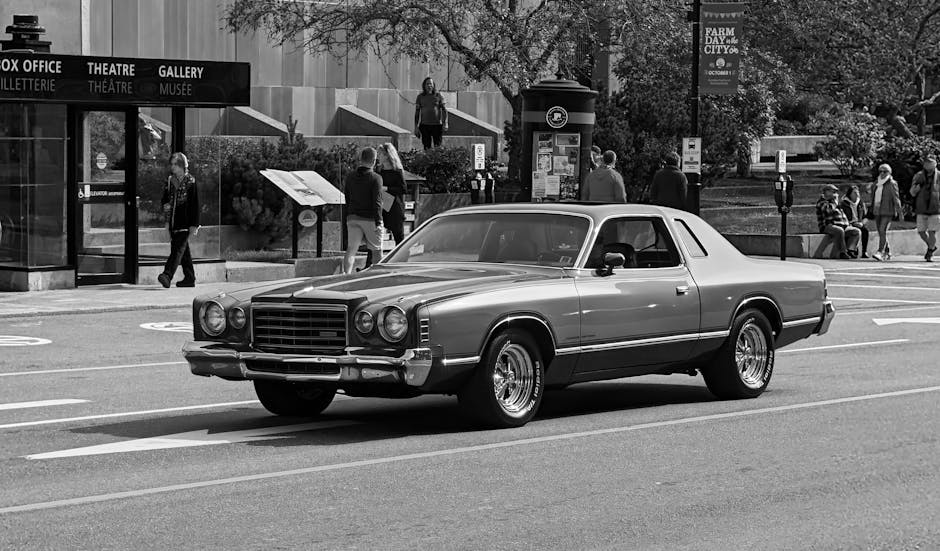Classic car driving through an urban street in Charlottetown, Canada, captured in black and white.