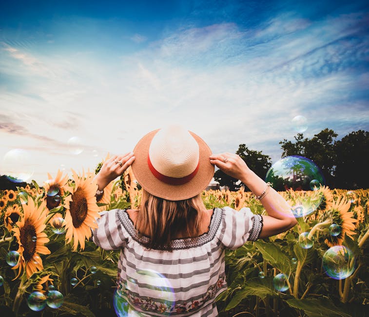 A woman stands in a vibrant sunflower field, enjoying the summer day with bubbles floating around.