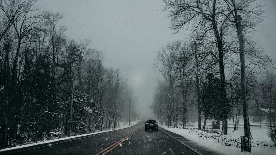 A lone car travels a snow-covered road through a barren winter landscape in Kitchener, Ontario. Crisp and serene.