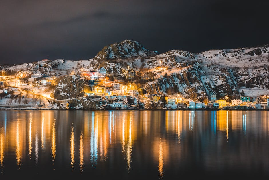 Enchanting night scene of St. John's harbor with illuminated houses and reflections on water.