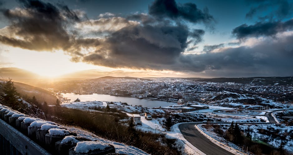 Stunning aerial view of St. John's, NL, Canada at winter sunset, with snow, cityscape, and dramatic clouds.