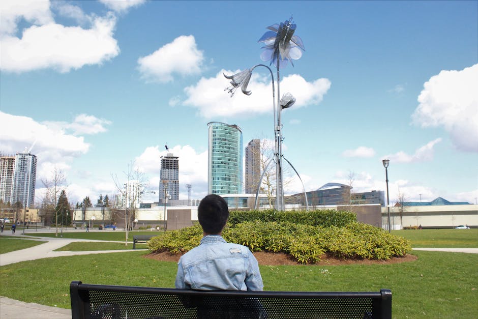 A person sits on a bench in Surrey, BC, observing the urban skyline and unique public art.