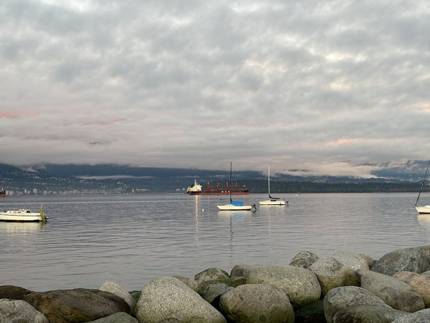 Peaceful scene of Vancouver harbour with sailboats and mountains under cloudy sky.